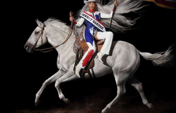 De zangeres Beyonce gekleed in rodeokleding op een wit galopperend paard, met in haar hand de Amerikaanse vlag en op haar hoofd een cowboyhoed.
